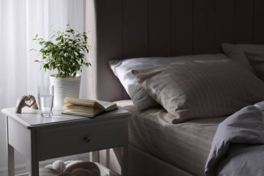 Yatağın yanında kitap, dekor ve bir bardak su olan komodin.