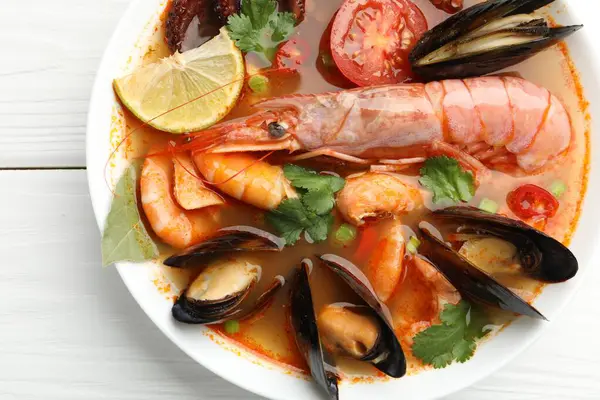 Lezzetli deniz ürünleri çorbası, beyaz ahşap masada, üst manzara.