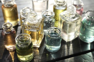 Siyah ahşap arka planda aromatik yağlı parfüm şişeleri, yakın plan.