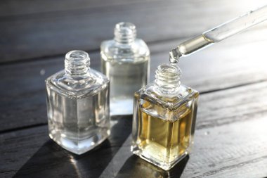 Siyah ahşap arka planda damlatan parfüm şişesinden aromatik yağ almak, yakın plan.