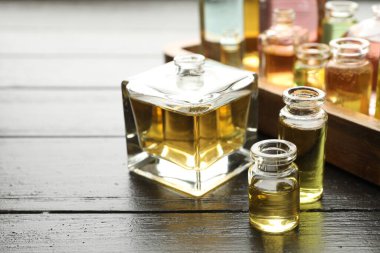 Siyah ahşap arka planda aromatik yağlı parfüm şişeleri, yakın plan.