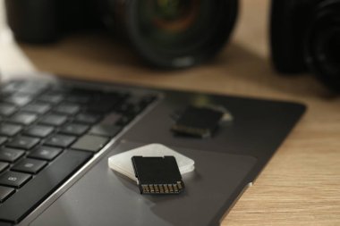 SD hafıza kartları, tutucu, dizüstü bilgisayar ve fotoğraf makinesi ahşap masada, yakın plan.