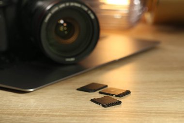 SD hafıza kartları, dizüstü bilgisayar ve fotoğraf makinesi ahşap masada, yakın plan.