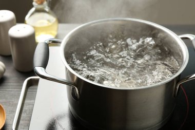 Kaynar suyla pişirme tenceresi ve ahşap masa üzerinde gri arka plan, yakın çekim