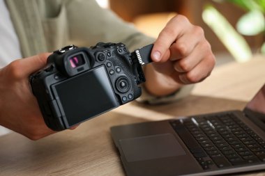 SD hafıza kartını ahşap masadaki fotoğraf makinesine yerleştiren adam, yakın plan.