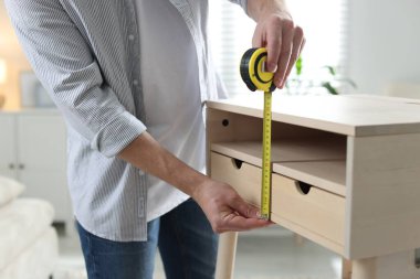 İçerideki bantla ahşap dolabı ölçen adam, yakın plan.