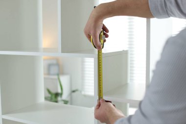 Beyaz rafları bantla ölçen adam içeride, yakın plan.