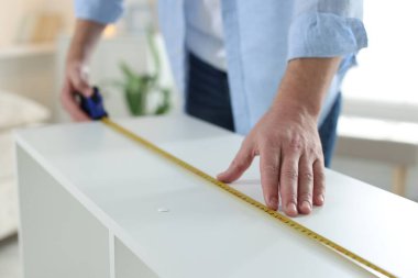 Beyaz rafları bantla ölçen adam içeride, yakın plan.