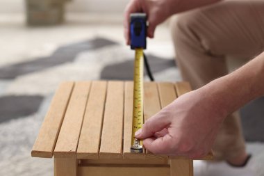 İçerideki bantla ahşap tabureyi ölçen adam, yakın plan.