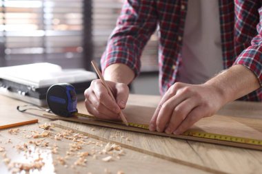 Kapalı alanda bant ile ahşap kalas ölçen bir adam.