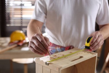 Kapalı alanda tahta rafı bant ve kalemle ölçen adam, yakın plan.