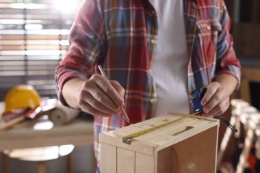 Kapalı alanda tahta rafı bant ve kalemle ölçen adam, yakın plan.