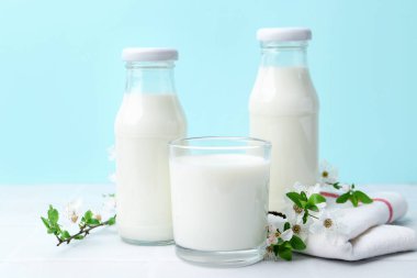 Taze süt ve çiçekler beyaz masada açık mavi arka planda