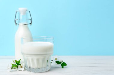 Taze süt ve çiçekler beyaz masada açık mavi arka planda. Metin için boşluk