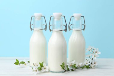 Taze süt ve çiçekler beyaz masada açık mavi arka planda