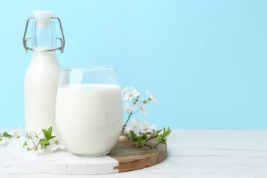 Taze süt ve çiçekler beyaz masada açık mavi arka planda. Metin için boşluk