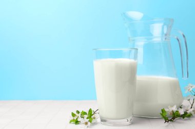 Taze süt ve çiçekler beyaz masada açık mavi arka planda. Metin için boşluk