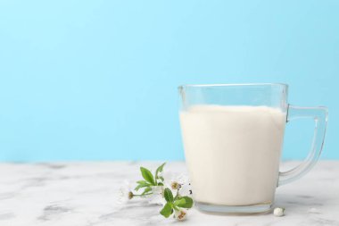 Açık mavi arka planda beyaz mermer masada bir fincan süt ve çiçek. Metin için boşluk