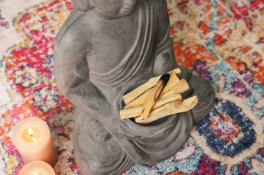 Palo santo sopalarıyla Buda heykeli ve kapalı alanda yanan mumlar.