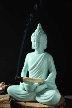Yanan palo santo sopası ve Buda heykeli siyah arka planda, yakın plan