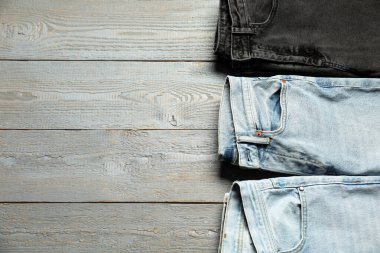 Different stylish jeans on grey wooden background, flat lay. Space for text