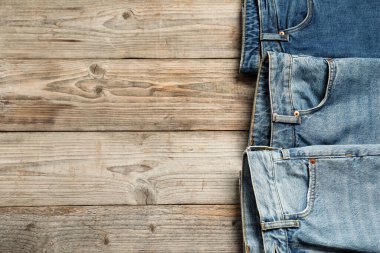 Different stylish jeans on wooden background, flat lay. Space for text