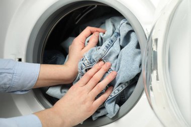 Kadın çamaşır makinesine kot pantolon koyuyor, yakın plan.