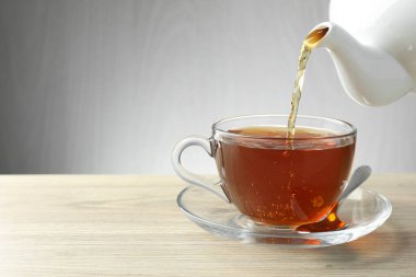 Ahşap masada çaydanlıktan fincana taze demlenmiş çay dökülüyor, yakın plan. Metin için boşluk