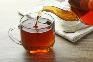 Tahta masada çaydanlıktan fincana taze demlenmiş çay dökülüyor, yakın plan.