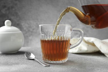 Gri masada çaydanlıktan fincana taze demlenmiş çay dökülüyor, yakın plan.