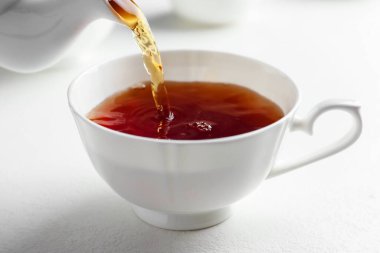 Beyaz masada çaydanlıktan fincana taze demlenmiş çay dökülüyor, yakın plan.