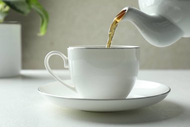 Beyaz masada çaydanlıktan fincana taze demlenmiş çay dökülüyor, yakın plan.