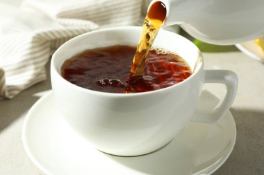 Hafif desenli masada çaydanlıktan fincana aromatik çay dökülüyor, yakın plan.