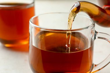 Aydınlık masada çaydanlıktan fincana aromatik çay dökülüyor, yakın plan.