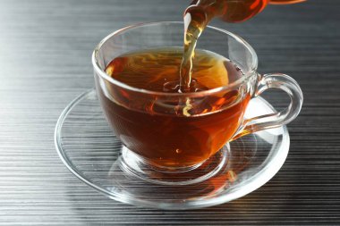 Siyah ahşap masada fincana aromatik çay dökülüyor, yakın plan.