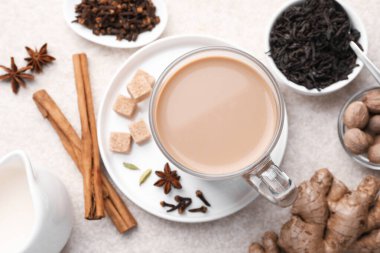 Cam bardakta Aromatik Masala çayı, beyaz desenli masada baharatlar ve kahverengi şeker, düz uzanmış.