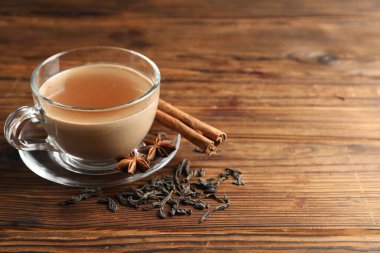 Bardakta Aromatik Masala çayı, ahşap masada baharatlar ve kuru yapraklar, yakın plan.