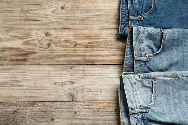 Different stylish jeans on wooden background, flat lay. Space for text