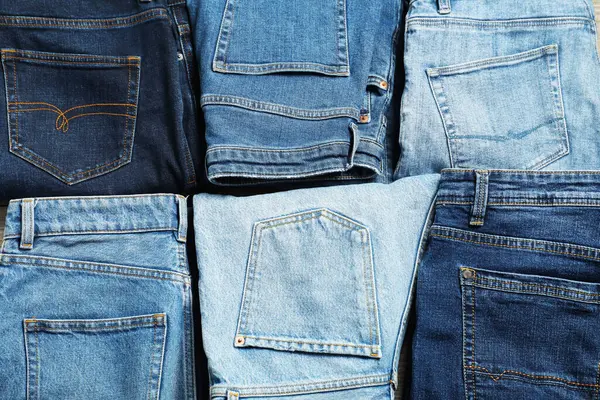 Different stylish jeans as background, top view