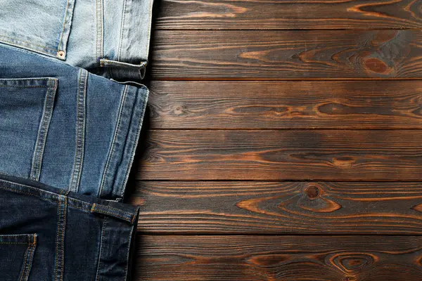 Different stylish jeans on wooden background, flat lay. Space for text
