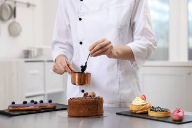 Pasta şefi pastayı eritilmiş çikolatayla süslüyor. Mutfakta, yakın plan.