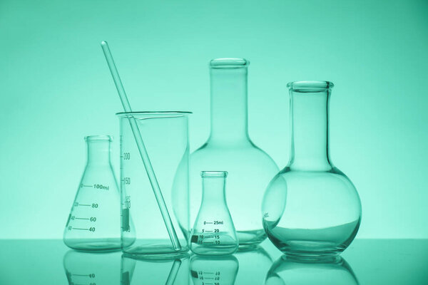 Laboratory glassware on mirror surface against green background