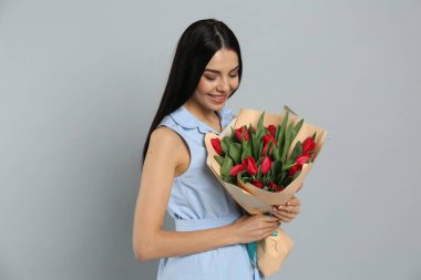Açık gri arka planda kırmızı lale çiçekli mutlu kadın. 8 Mart kutlamaları