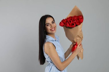 Açık gri arka planda kırmızı lale buketi olan mutlu bir kadın. 8 Mart kutlamaları