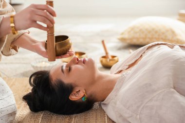 Şarkı söyleyen kadın kase terapisi görüyor. Kapalı yerde yatıyor.