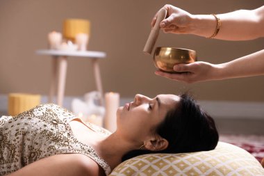 Şarkı söyleyen kadın kase terapisi görüyor. Kapalı yerde yatıyor.