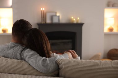 Çift kanepede, şık şömineli, arka manzaralı bir odada birlikte vakit geçiriyor.