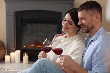 Mutlu çift evde şöminenin yanında kadeh tokuşturuyor.