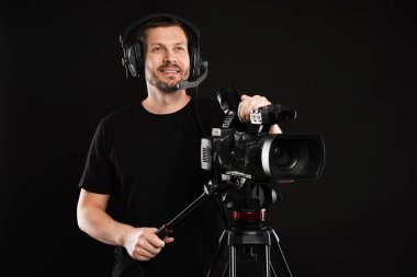 Profesyonel kameralı ve kulaklıklı bir adam siyah arka planda.