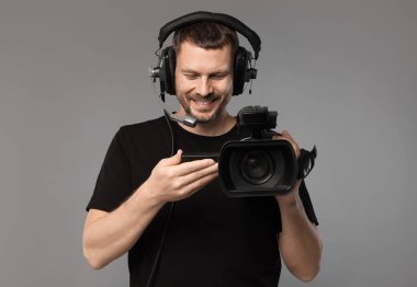 Profesyonel kameralı ve kulaklıklı bir adam gri arka planda.